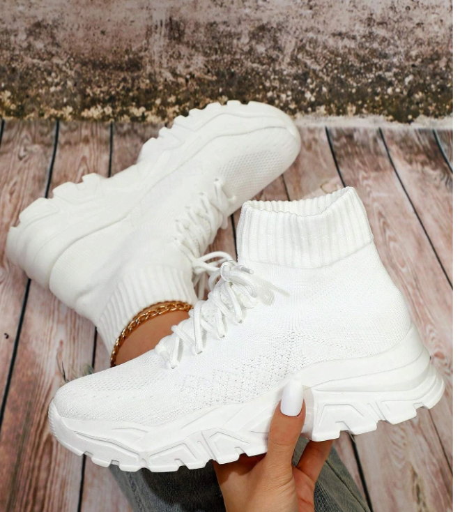 A person's hand holding a pair of white shoes